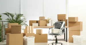 An office space filled with numerous cardboard boxes and packing materials, indicating a move or relocation process.